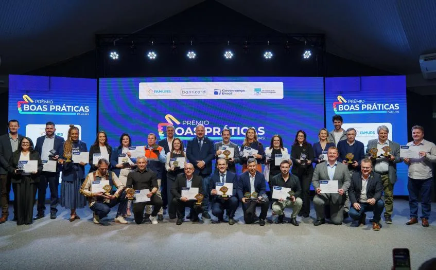Representantes dos municípios premiados reunidos no palco com troféus e certificados do 8º Prêmio Boas Práticas da Famurs.